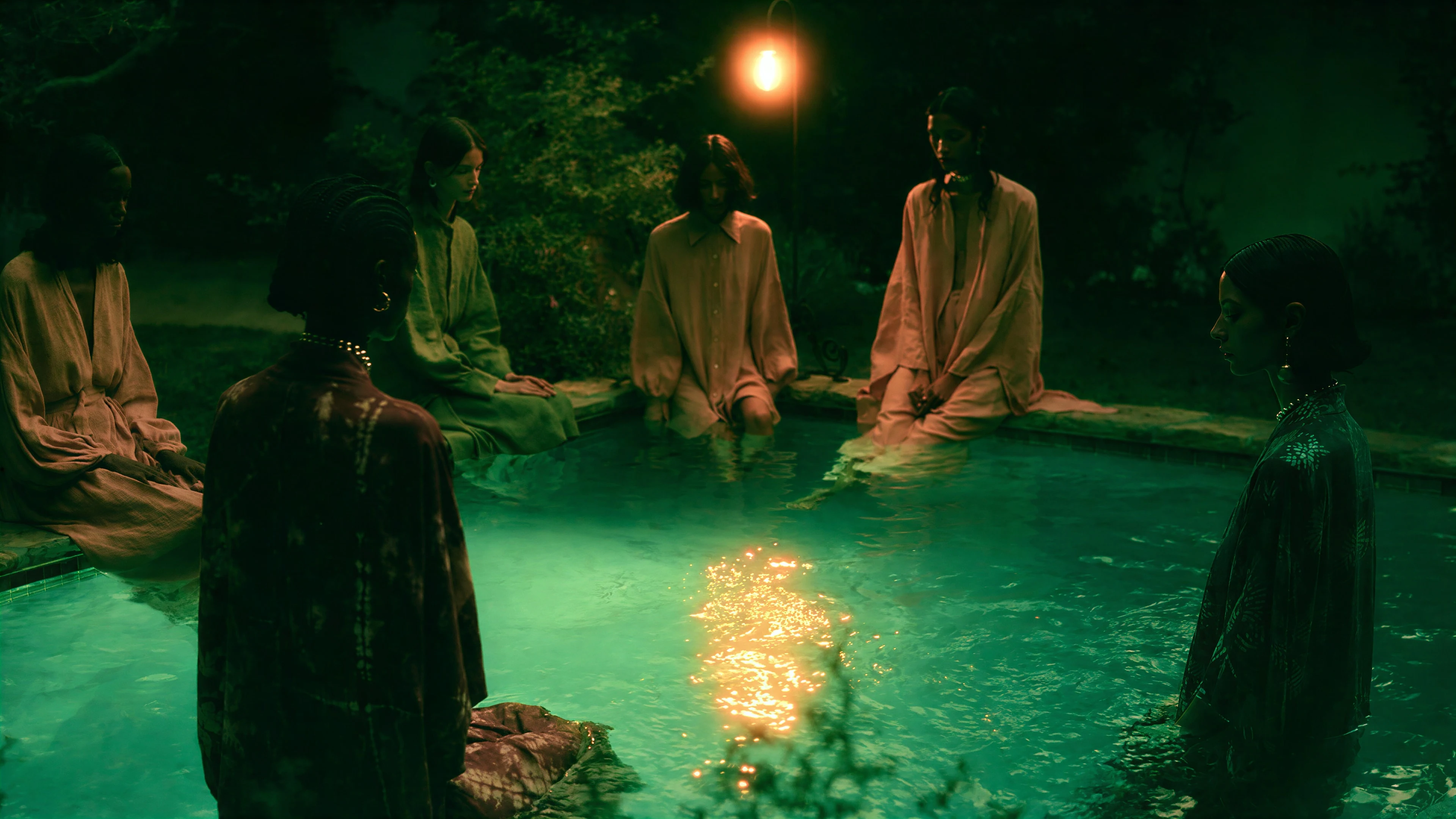 Four models gathered around a glowing pool at night